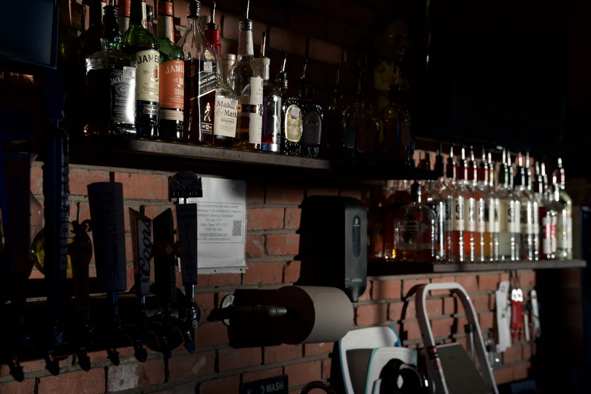 The back bar in low light, whiskey shelf and tap handles against the brick