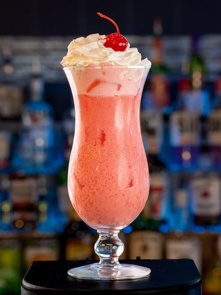 The Beachy Sunrise, a creamy pink cocktail with whipped cream and a cherry