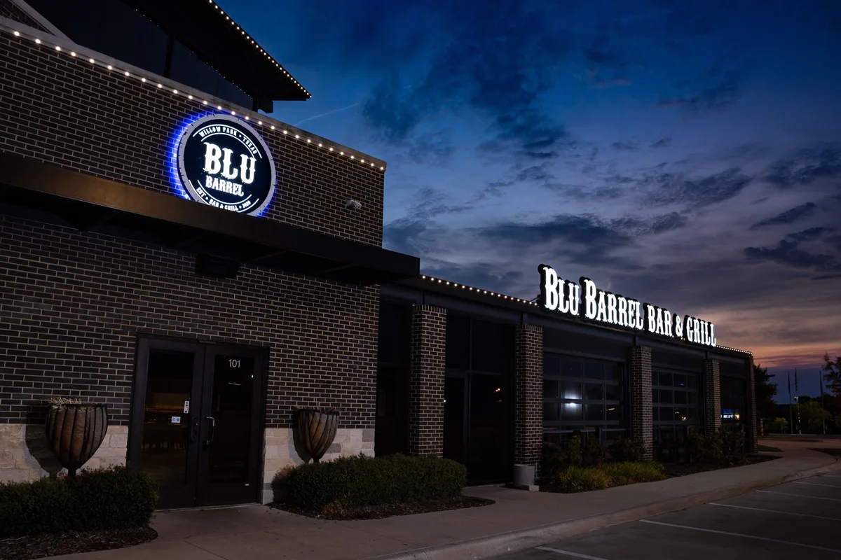 The Blu Barrel Bar and Grill building at dusk, the blue BLU BARREL medallion lit on the brick