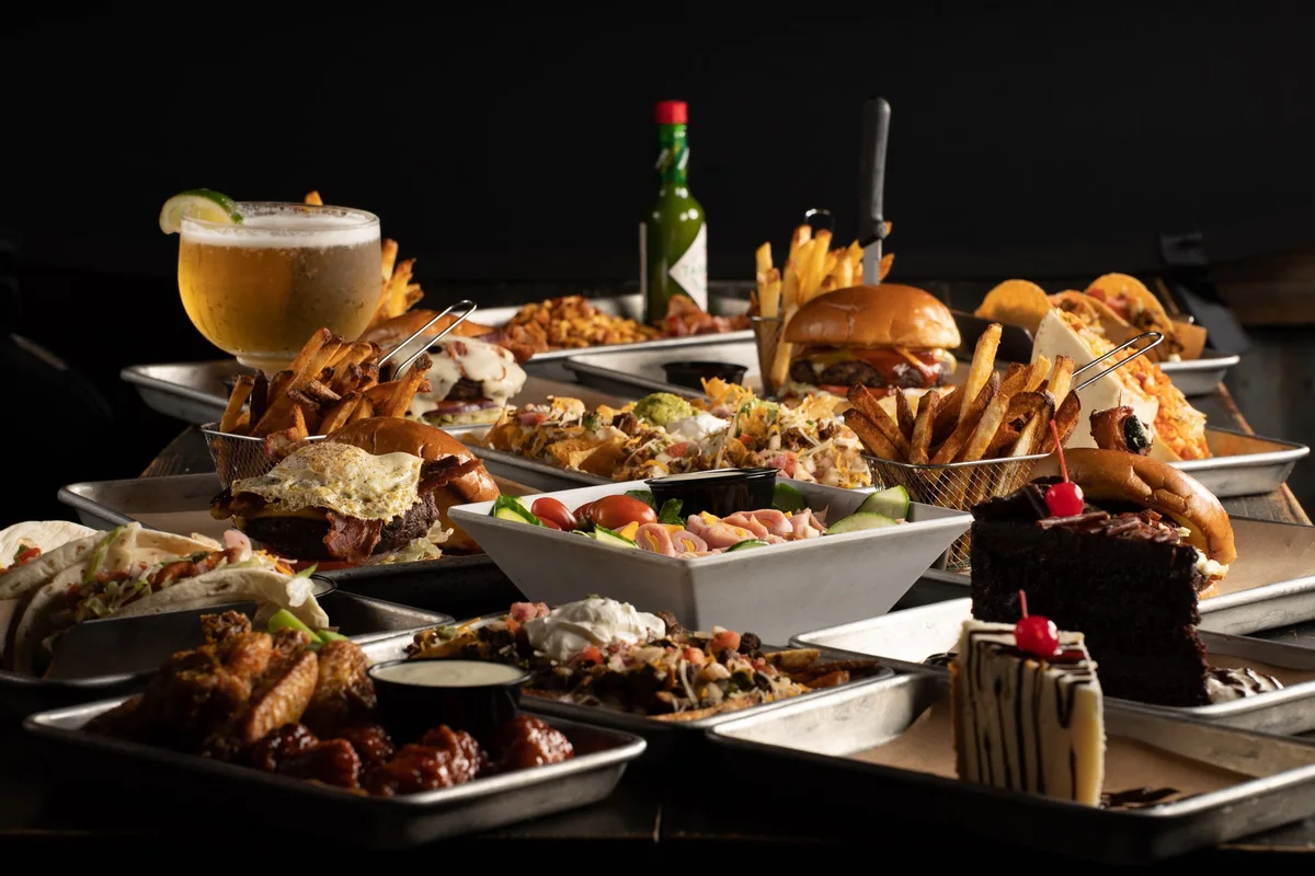 A full spread of Blu Barrel trays: burgers, wings, nachos, tacos, desserts and a cold draft beer